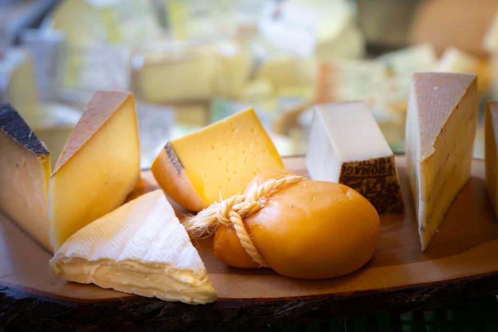 Vier Sorten Hartkäse auf Holzbrett mit Käsetheke im Hintergrund